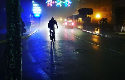 Rear view of silhouette man walking on illuminated street at night