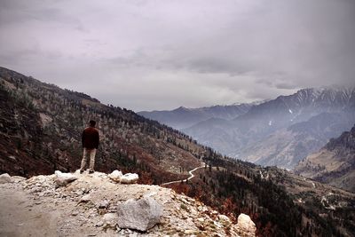 Rear view of man standing on mountain against sky