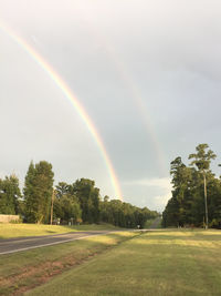 Scenic view of rainbow over trees on field against sky