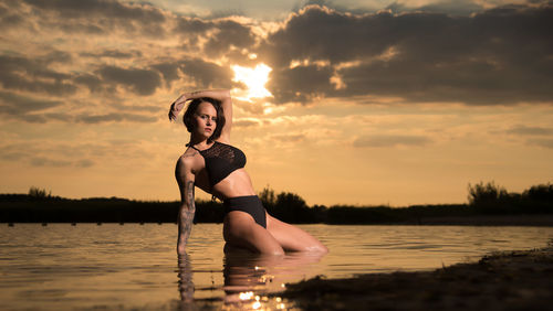 Young woman in lake against sky during sunset