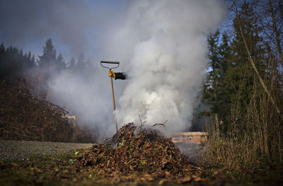 Person with gardening equipment surrounded by smoke emitting from burned leaves person