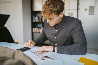 Young blond male student using calculator while studying in community college