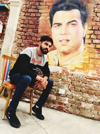 Portrait of young couple sitting against brick wall