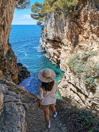 Young woman in summer outfit standing on cliff above sea.