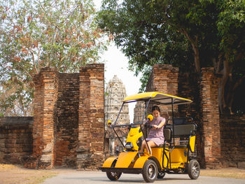 Woman wearing purple dress on electric car and old temple at sukhothai, thailand in march 13 2021