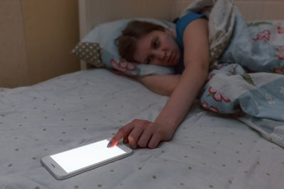 High angle view of cute girl using mobile phone while lying on bed at home