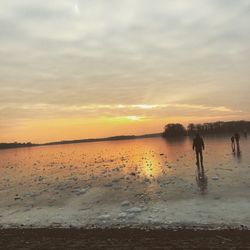 Silhouette men on beach against sky during sunset