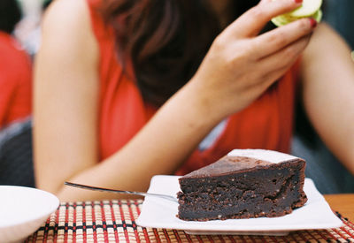 Midsection of woman with chocolate cake slice served in plate at restaurant