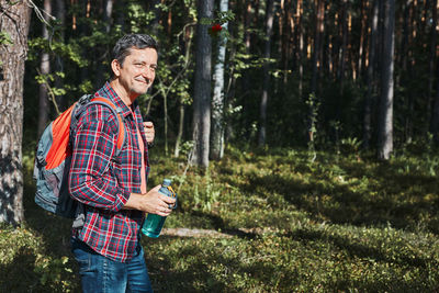 Man with backpack hiking in forest, actively spending vacations enjoying hike on sunny vacation day