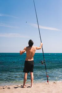 Rear view of shirtless man on beach against sky