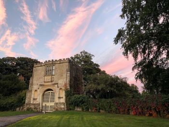 Built structure by trees against sky during sunset