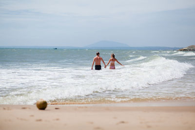 Rear view of couple standing in sea against sky