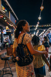 Smiling woman carrying backpack and exploring food market with daughter on vacation