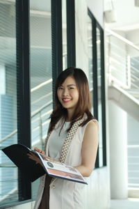 Portrait of smiling businesswoman holding file while standing in office
