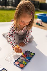 Focused child with mother painting with poster paint outdoors on the ground on big sheet of paper. 