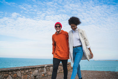 Cheerful friends walking by sea against sky