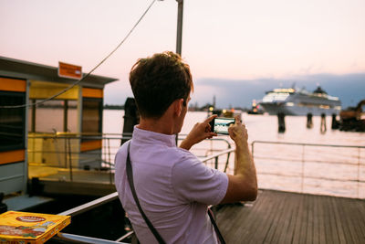 Man photographing with smart phone against sky during sunset