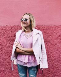 Portrait of young woman in sunglasses standing against pink wall