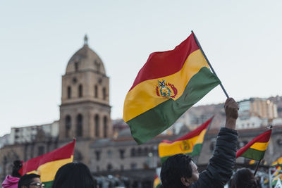 People with flags in front of building against sky during protest