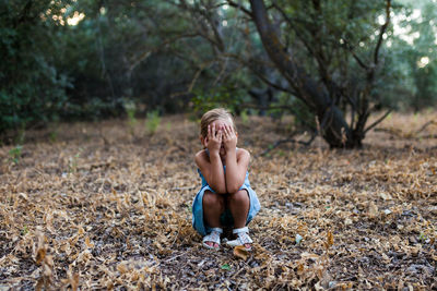 Girl covering face while crouching in forest