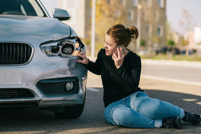 Young woman sitting on car in city