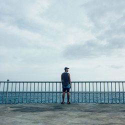 Man standing on railing against sea