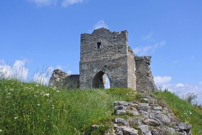 Low angle view of old ruin on hill against blue sky