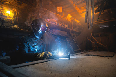 Welder in a workshop welds a metal part. general plan of an old cluttered garage where a man in