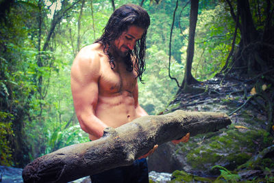 Shirtless young man carrying log in forest