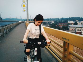 Woman riding bicycle on bridge against clear sky
