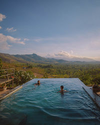 People in swimming pool by mountain against sky