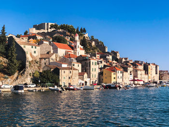 Buildings by sea against clear blue sky