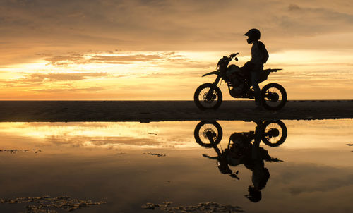 Man riding motorcycle on sea against sky during sunset