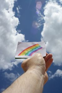 Person holding rainbow against sky