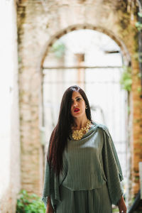 Portrait of young woman standing against building