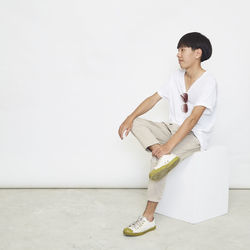 Young man looking away while standing against white wall