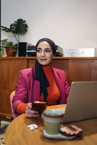 Young woman using mobile phone while sitting on table