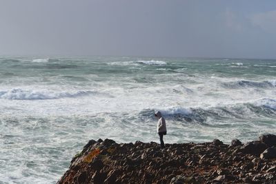 Side view of man standing on rock by sea against sky