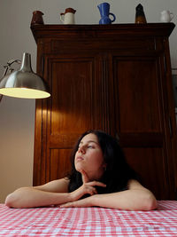 Portrait of young woman looking away while sitting on table