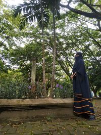 Rear view of man standing by trees in forest