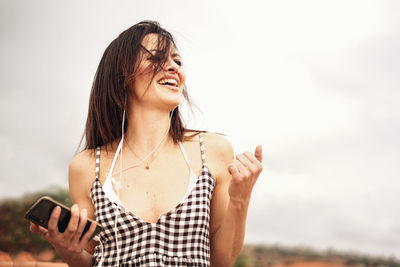 Happy woman listening music against sky