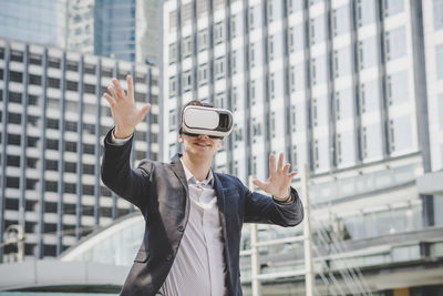 Businessman looking through virtual reality simulator while standing against building