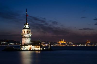 Illuminated maiden tower amidst sea against sky during sunset