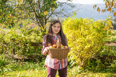 Portrait of girl holding fruits in basket at garden