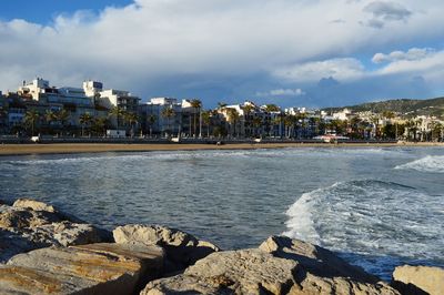View of city at waterfront against cloudy sky