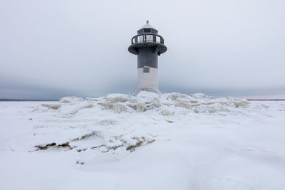 Lighthouse by sea against sky during winter