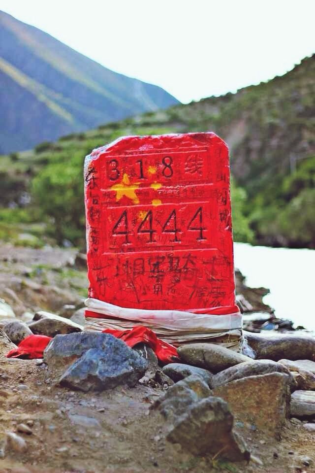 red, text, western script, communication, focus on foreground, rock - object, close-up, day, outdoors, guidance, sign, no people, non-western script, wall - building feature, mountain, warning sign, built structure, nature, information sign, capital letter