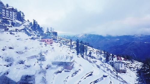 Snow covered houses by mountain against sky