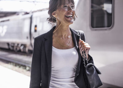 Happy businesswoman looking away while standing on railroad station