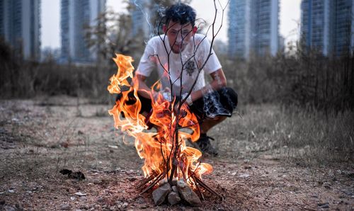 Portrait of young man crouching by fire on field